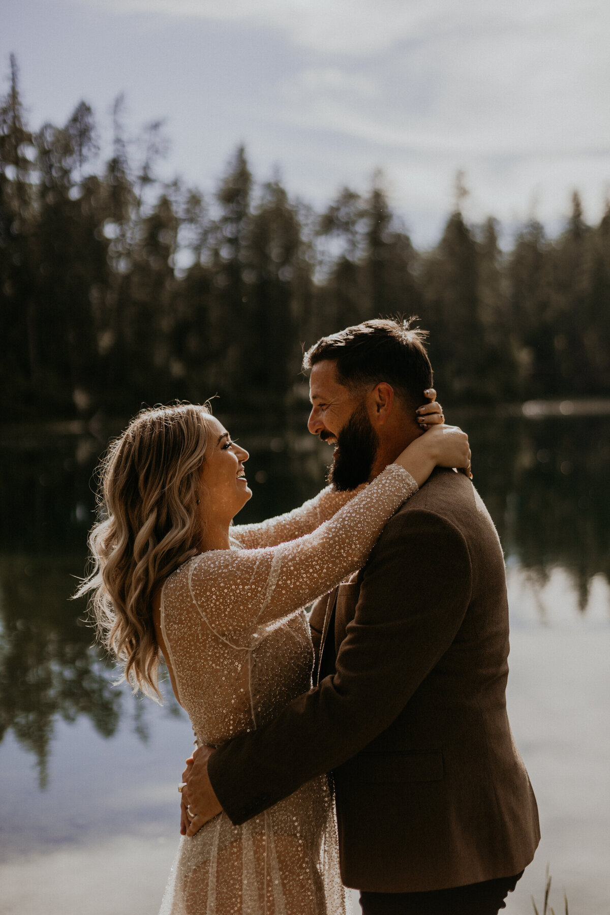 bride and groom holding each other and smiling in front of a lake in Montana