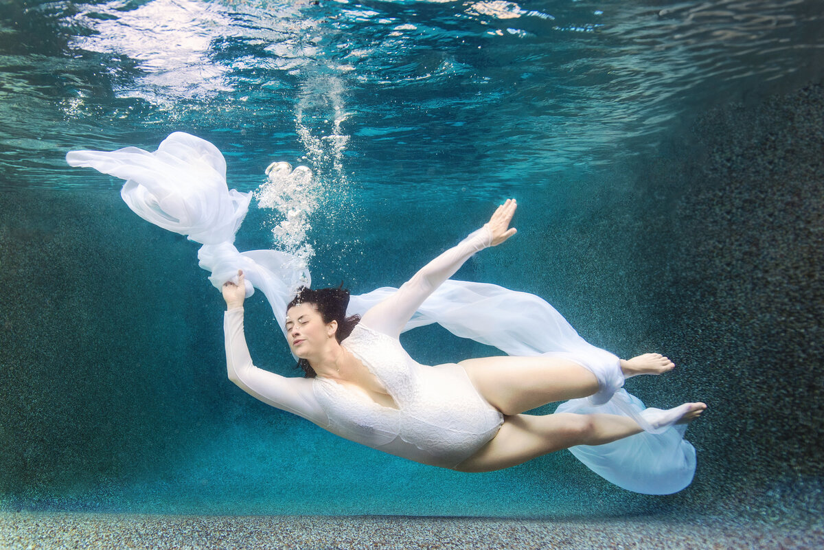 st-louis-underwater-photographer-pregnant-mom-underwater-in-white-bodysuit-and-white-fabric-and-blue-water