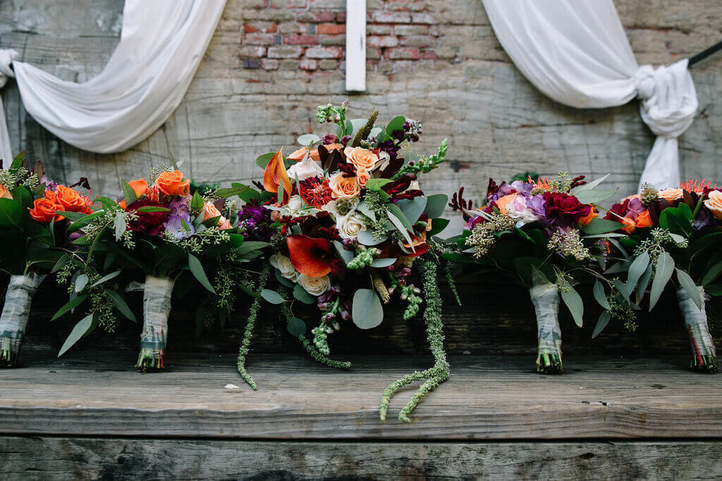 Several vibrant floral bouquets featuring roses, eucalyptus, and other colorful flowers are lined up on a wooden landing.