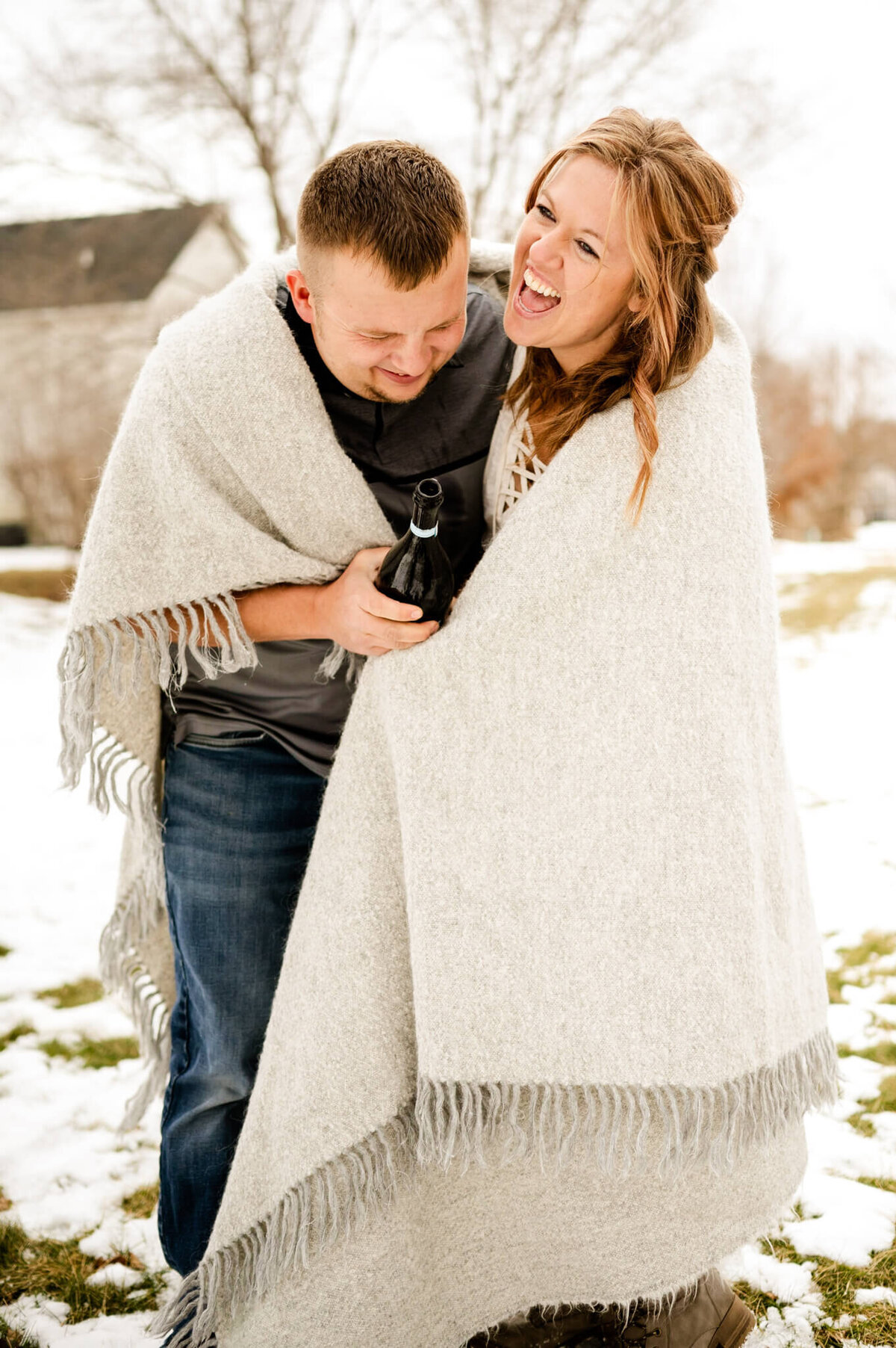 Married couple popping champagne outside in the winter while wrapped up in a blanket at a couples session near Chicago, IL.