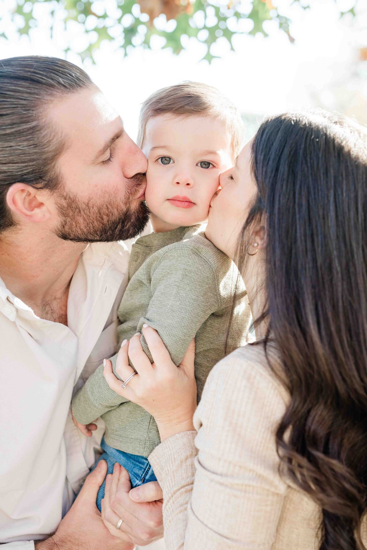 parents kissing their young son's cheeks