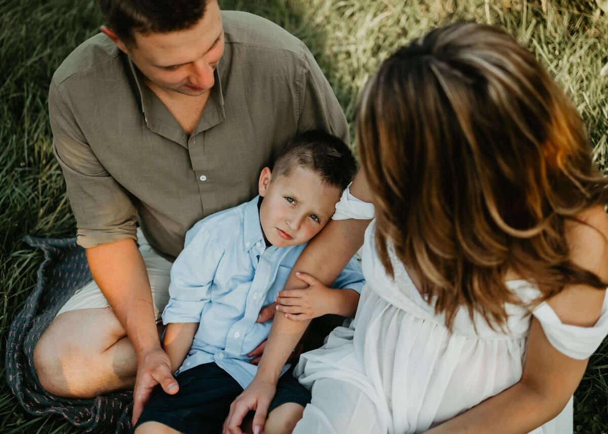 A family with their son sitting on a grassy field, captured by a Pittsburgh maternity photographer.