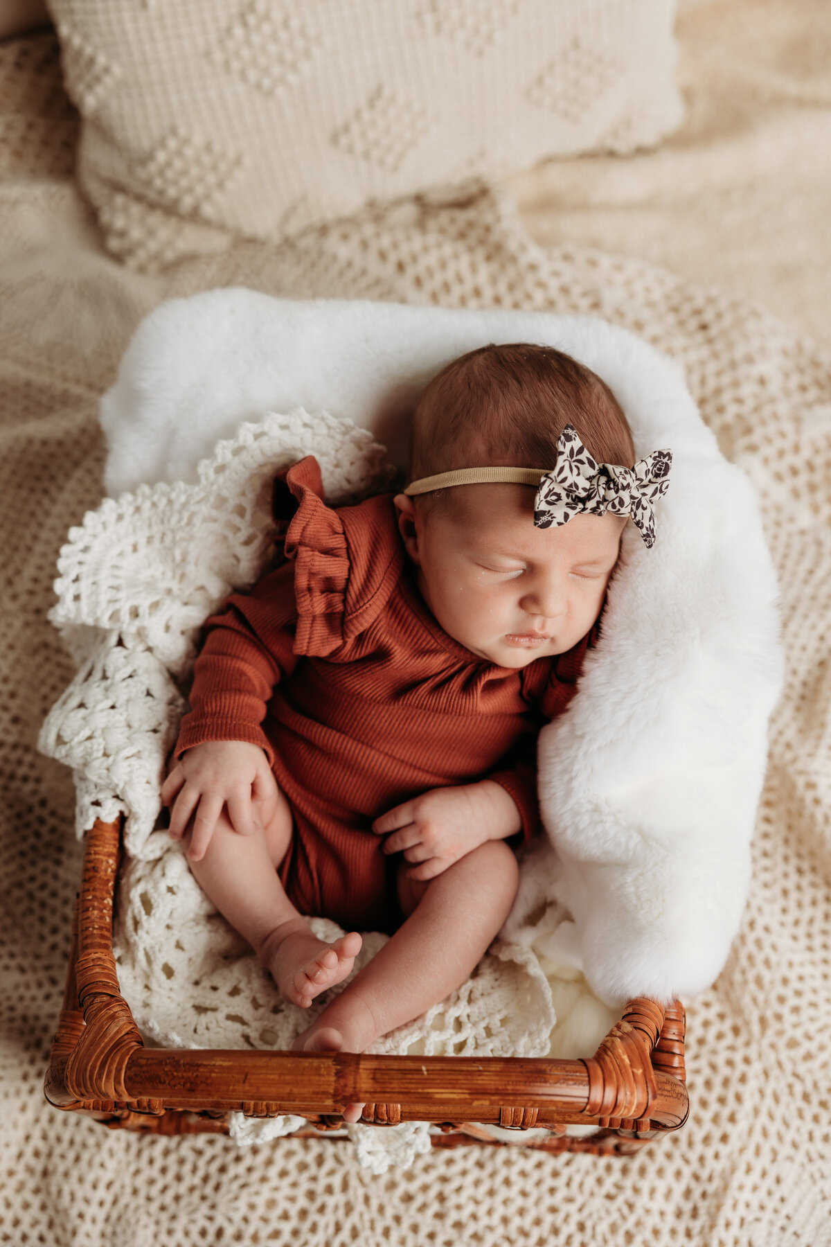 preciious newborn in a rust orange long sleeve onsie, wearing a black and white bow.