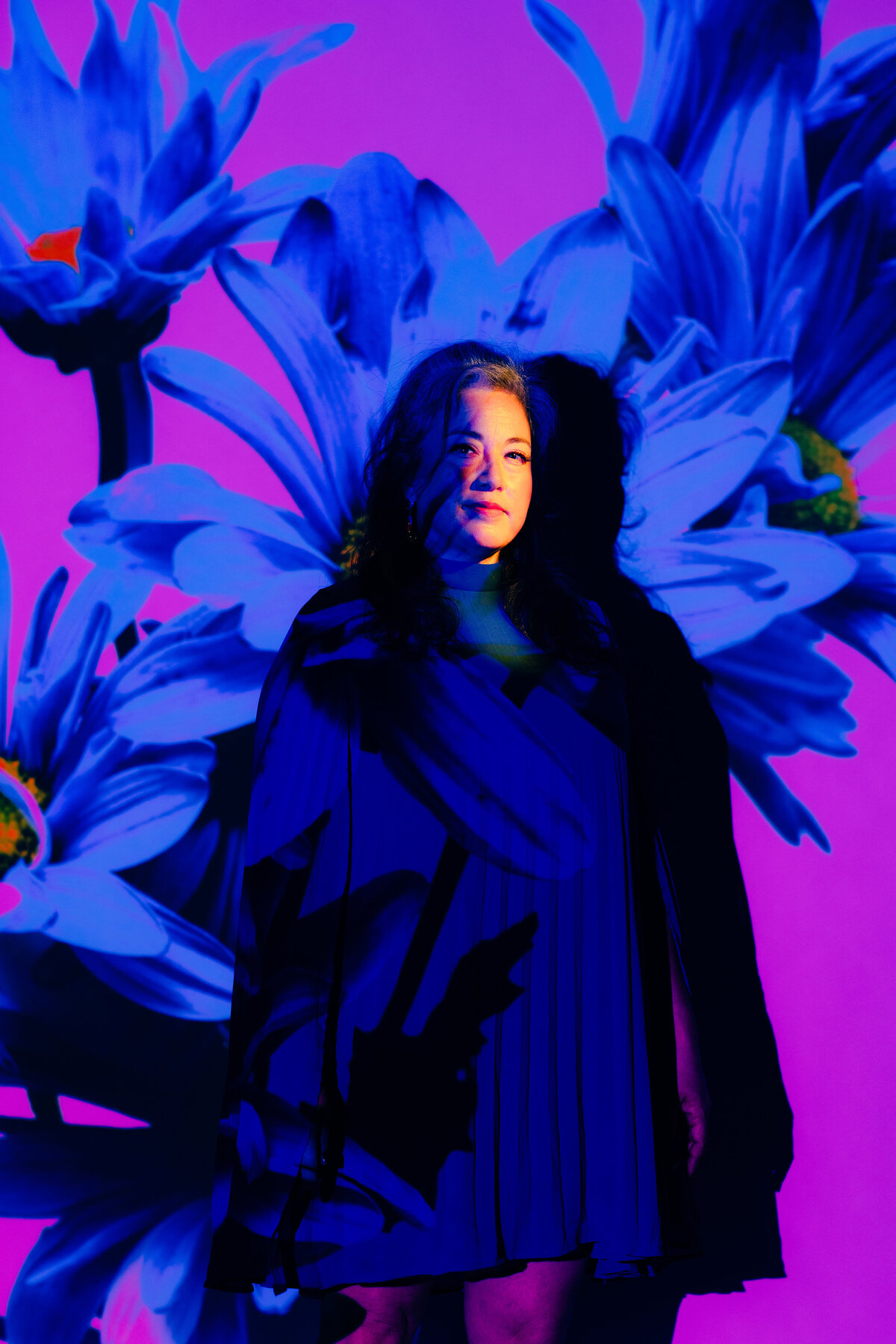 Woman in front of purple studio background with blue flowers projected over her
