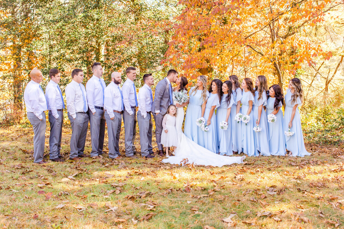 bridal party in fall foliage with bride and groom kissing