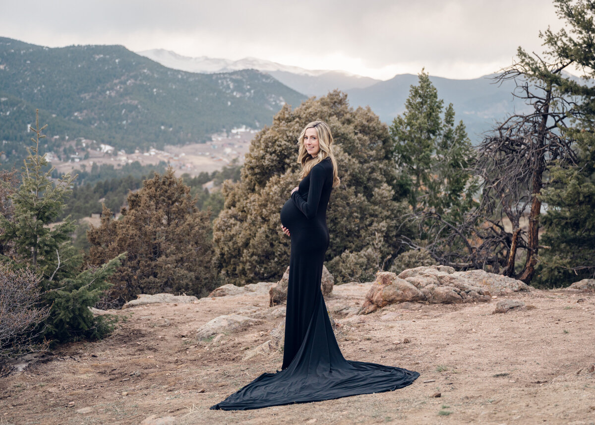 Pregnant woman in a long black dress standing in front of the mountains- photo by maegan r photography