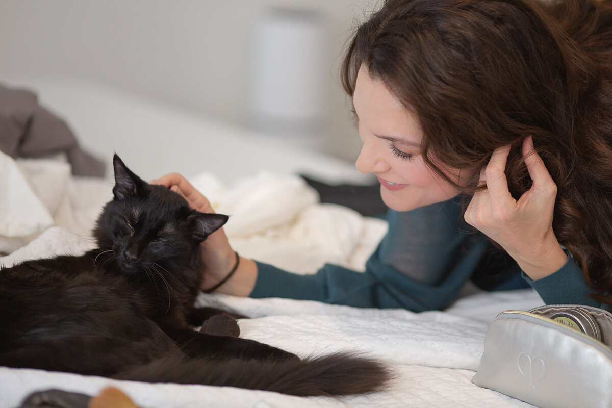 informal portrait of woman petting her cat on a bed