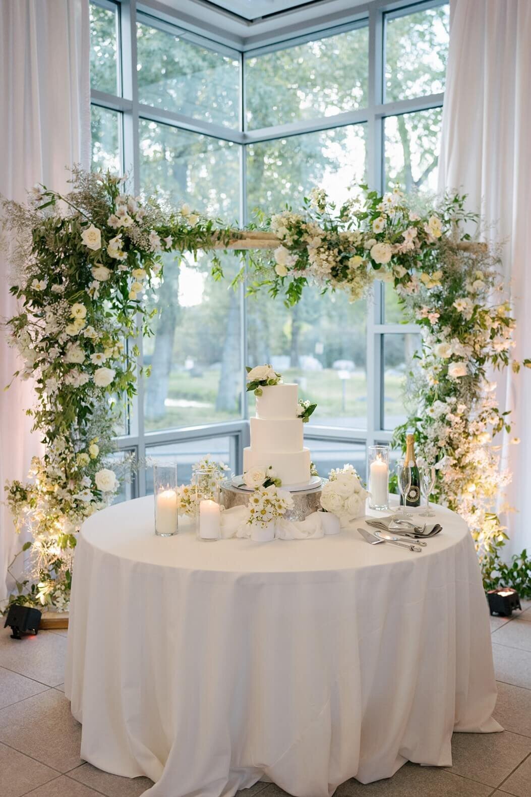 A beautiful white wedding cake adorned with simply elegant white florals and greenery sitting atop a cake table at the Aspen Meadows Resort wedding reception venue.