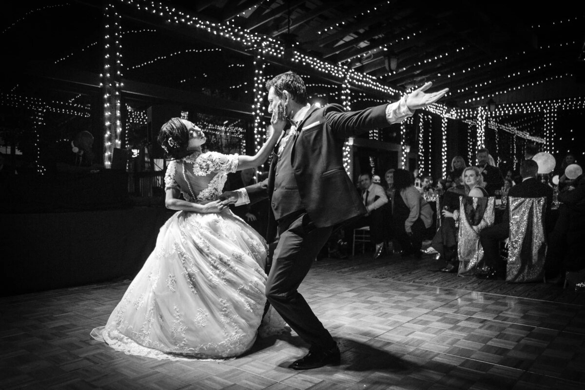 A dynamic black and white photo of the bride and groom dancing, their joyous movement mirrored by the sparkling lights above.