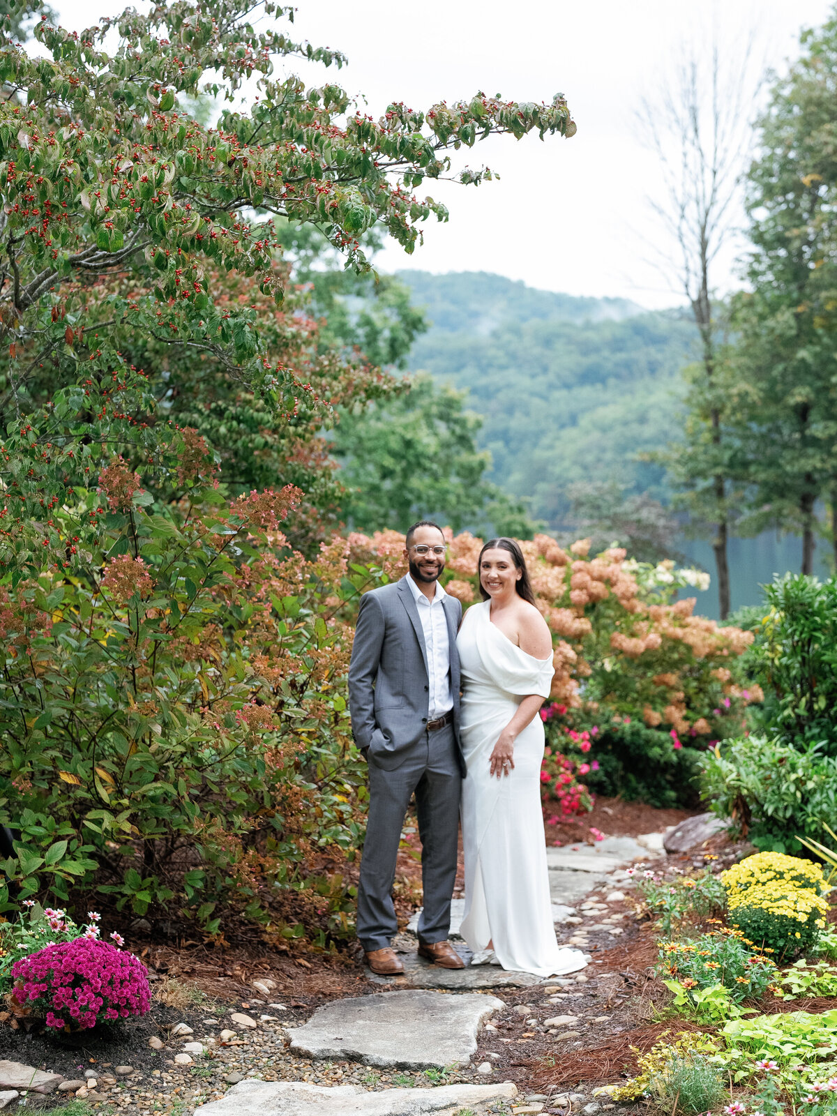 Bride and groom standing along a mountain garden path surrounded by fall foliage near Castle Ladyhawke in Tuckasegee, NC.