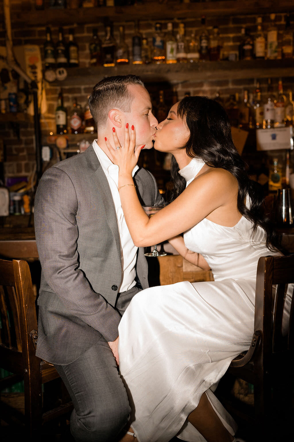 bride and groom sitting in chairs at a bar kissing each other