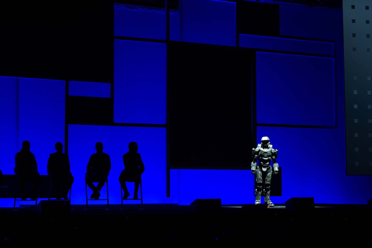 A robot illuminated on stage with geometric shapes darken behind it