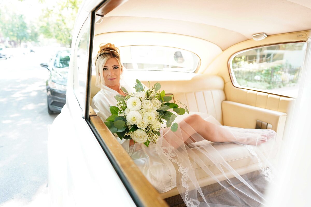 A bride sits elegantly in a car, showcasing her bridal attire in a refined and sophisticated setting. This image captures the bride’s grace and the details of her gown, highlighting the blend of classic elegance and modern luxury in her bridal portrait.