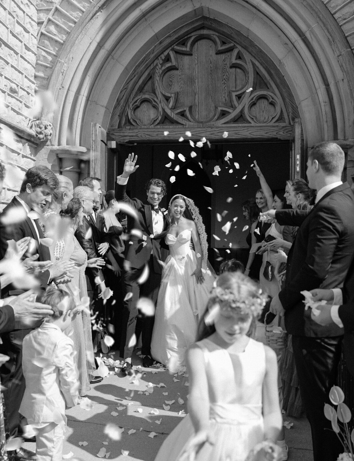 white rose petals fill the air as a couple runs outside after their wedding at Christ Church, Detroit