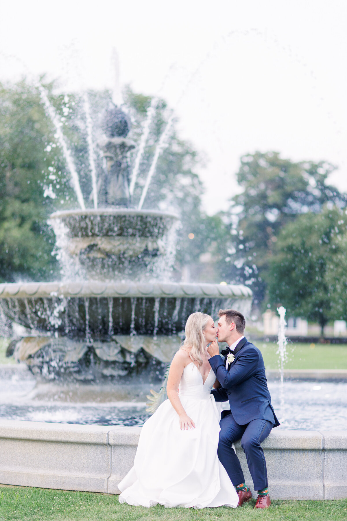 Bride and groom sitting and kissing in front of a fountain representing romantic Boston wedding photography