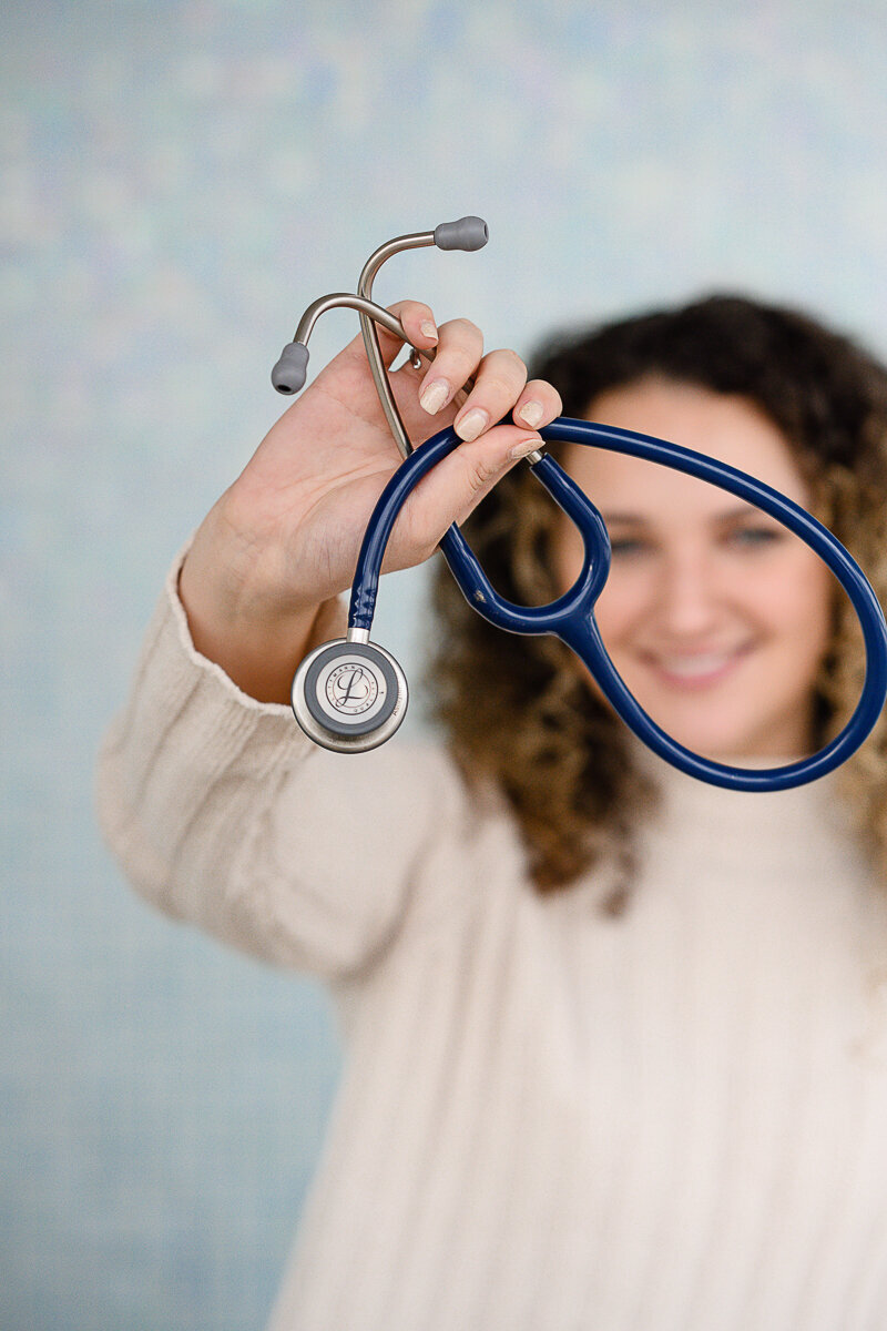 A branding photographer and commercial photographer takes a picture of a nurse holding up a stethoscope during a brand photoshoot for brand photos.