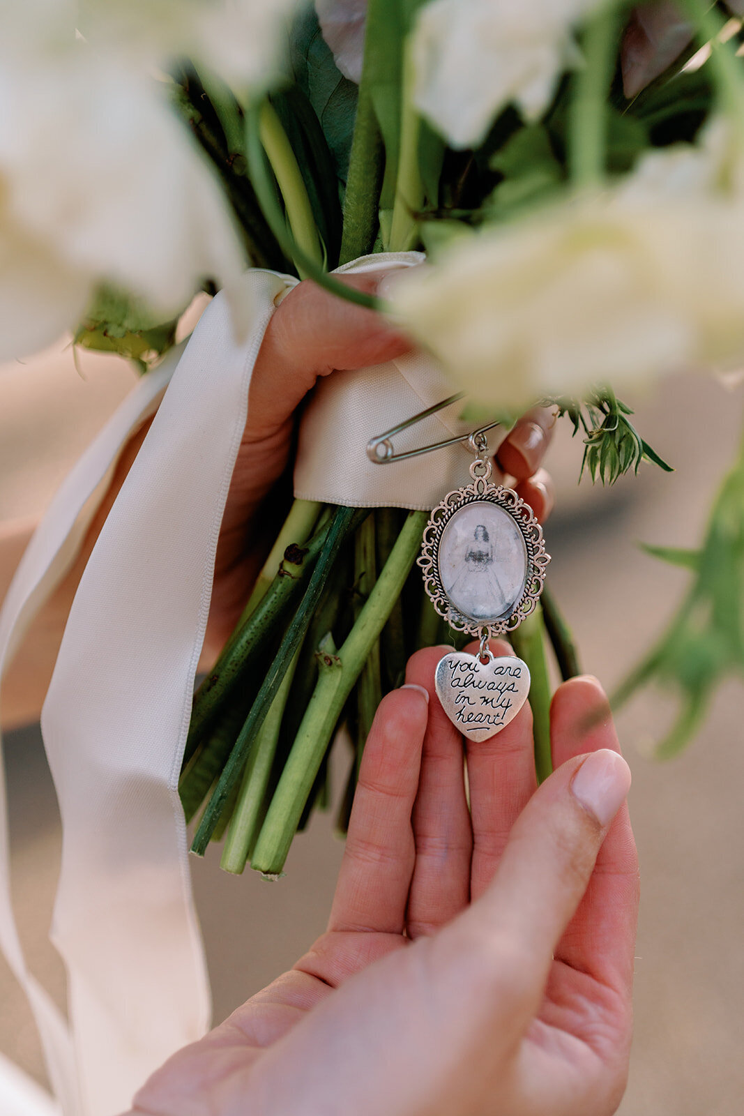 Close-up of bride holding wedding bouquet with sentimental photo charm and engraved heart locket reading “You are always in my heart,” captured during an elegant Huntsville wedding ceremony.