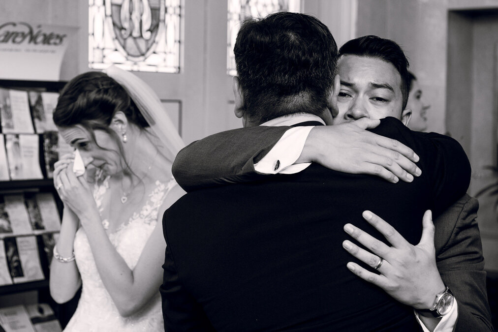 A bride crying as a two men embrace.