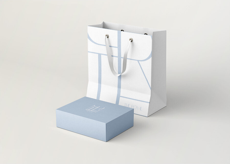 A blue and white branded shopping bag and matching box on a beige background.