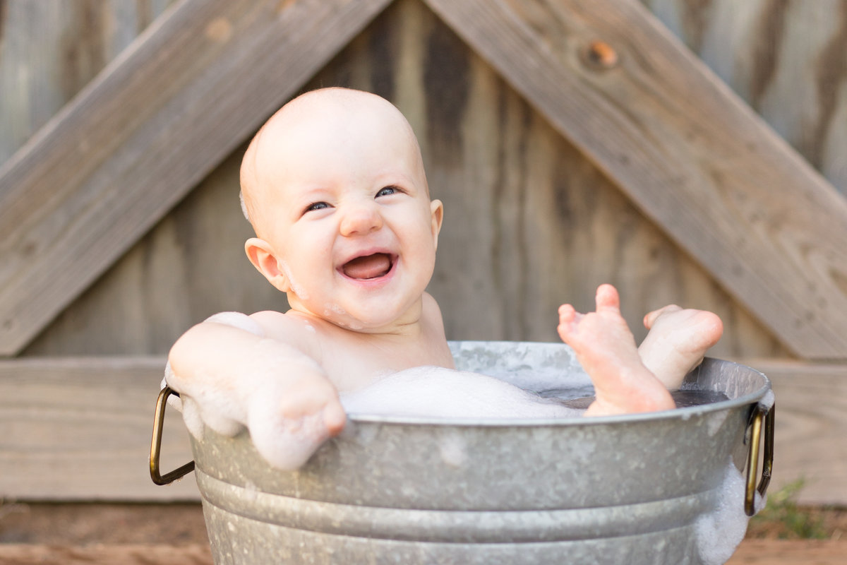 baby smiles in a bucket bath of bubbles