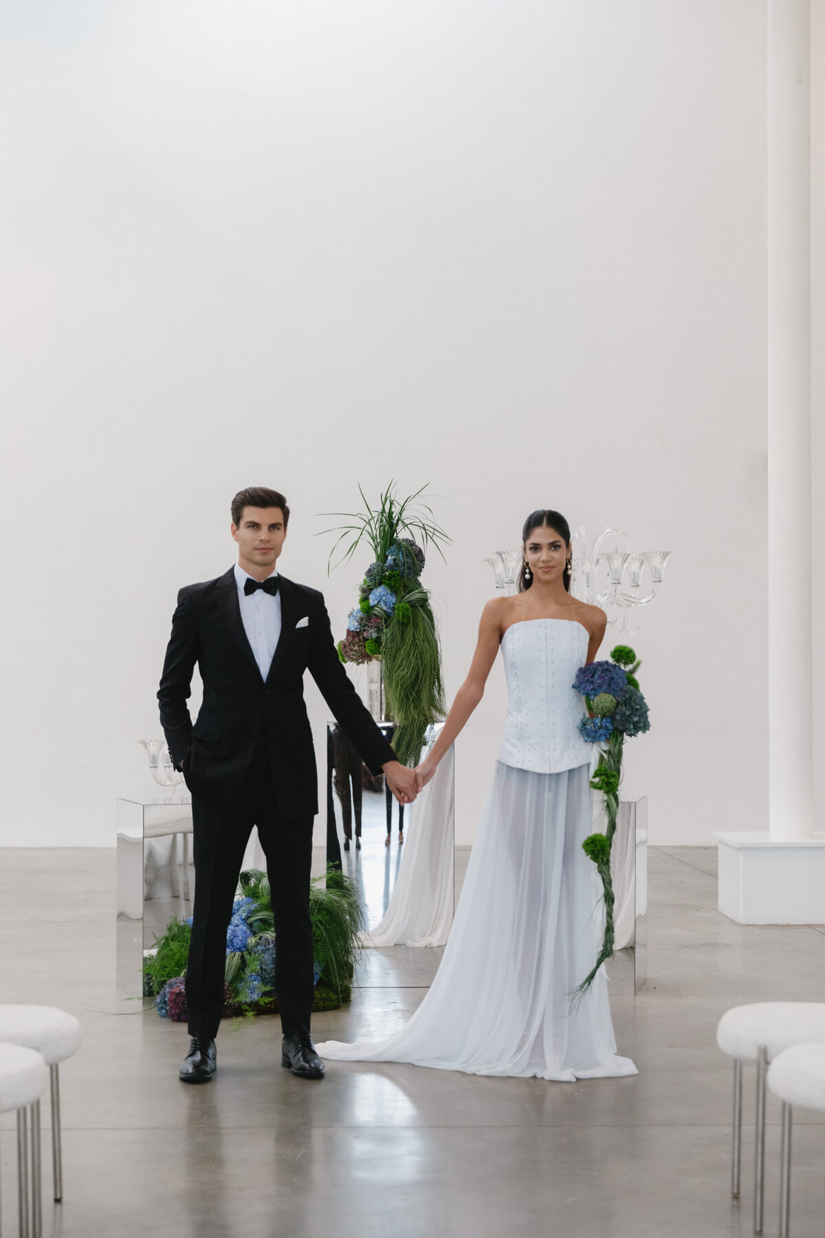 Bride and groom holding hands during an editorial wedding photoshoot at Sound River Studios in New York City, surrounded by modern florals and minimalist decor.