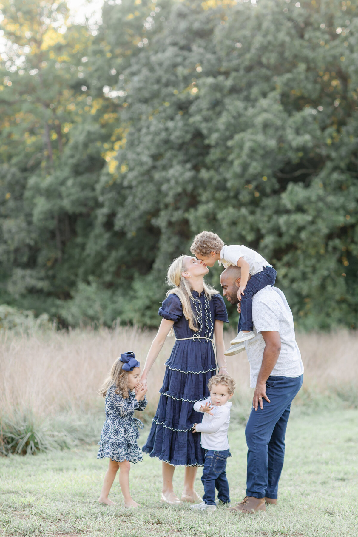 dad with child on shoulders bending over to kiss mom