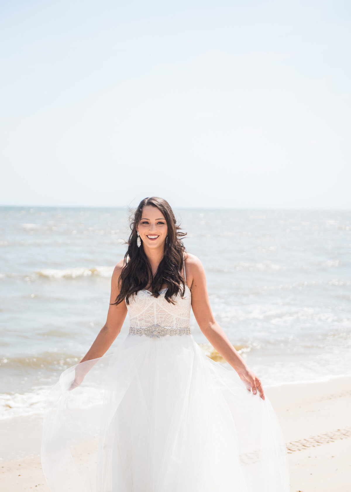 A person in a wedding dress standing at the edge of the ocean 