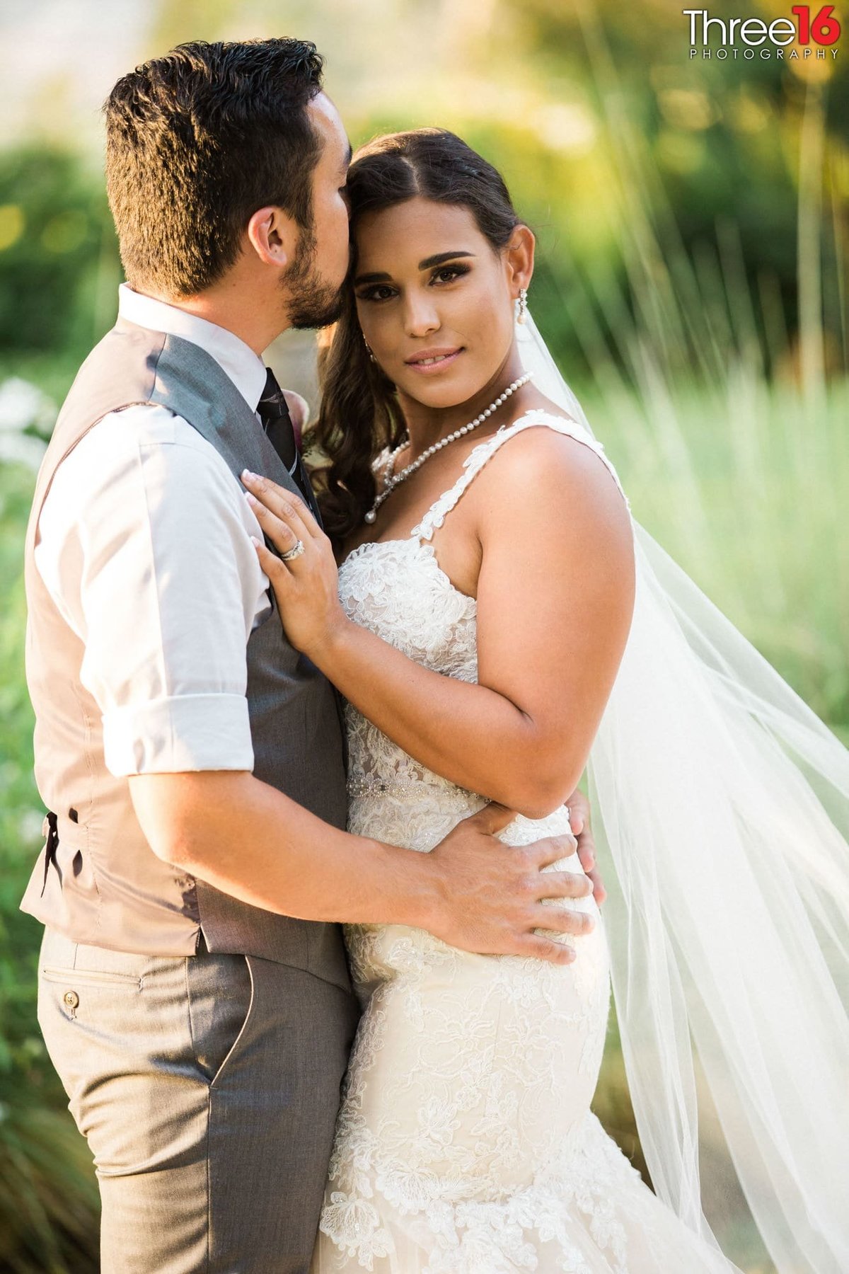 Grooms kisses Bride as she poses