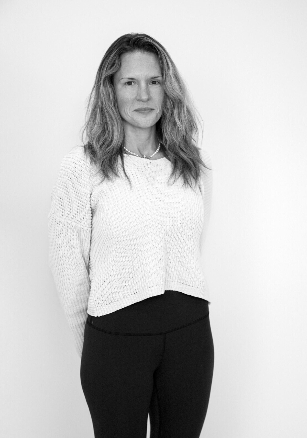 Black and white before shot of a woman in a sweater, smiling naturally against a plain white background. Studio before shot o