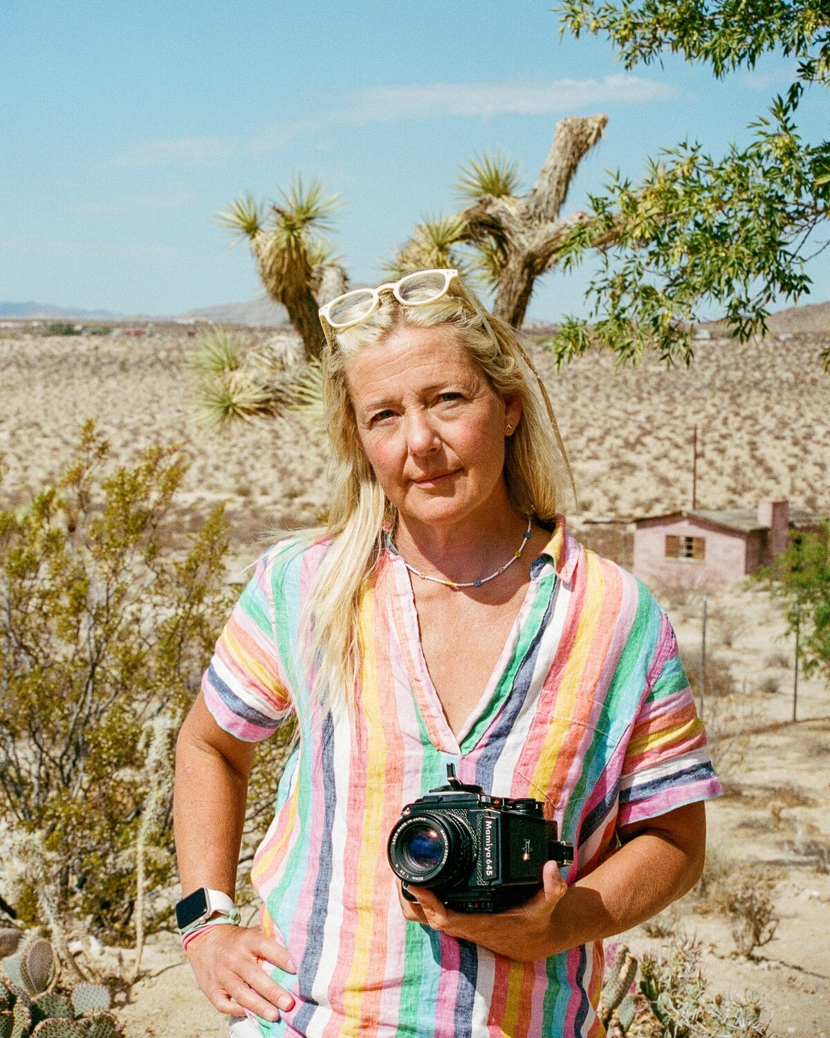 Woman holds her camera and gazes at the photographer with desert landscape in the background