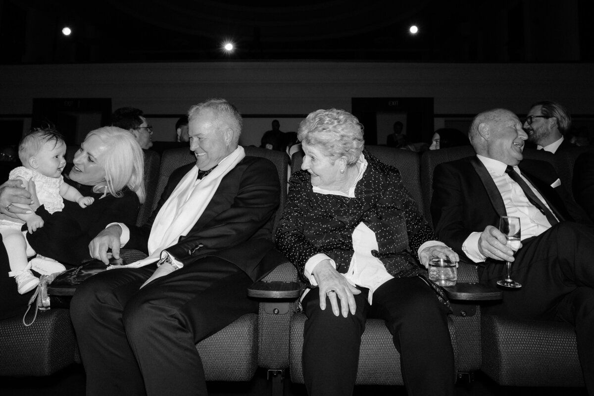 Black and white photo of guests sitting on cinema chairs at a regal cinema wedding.