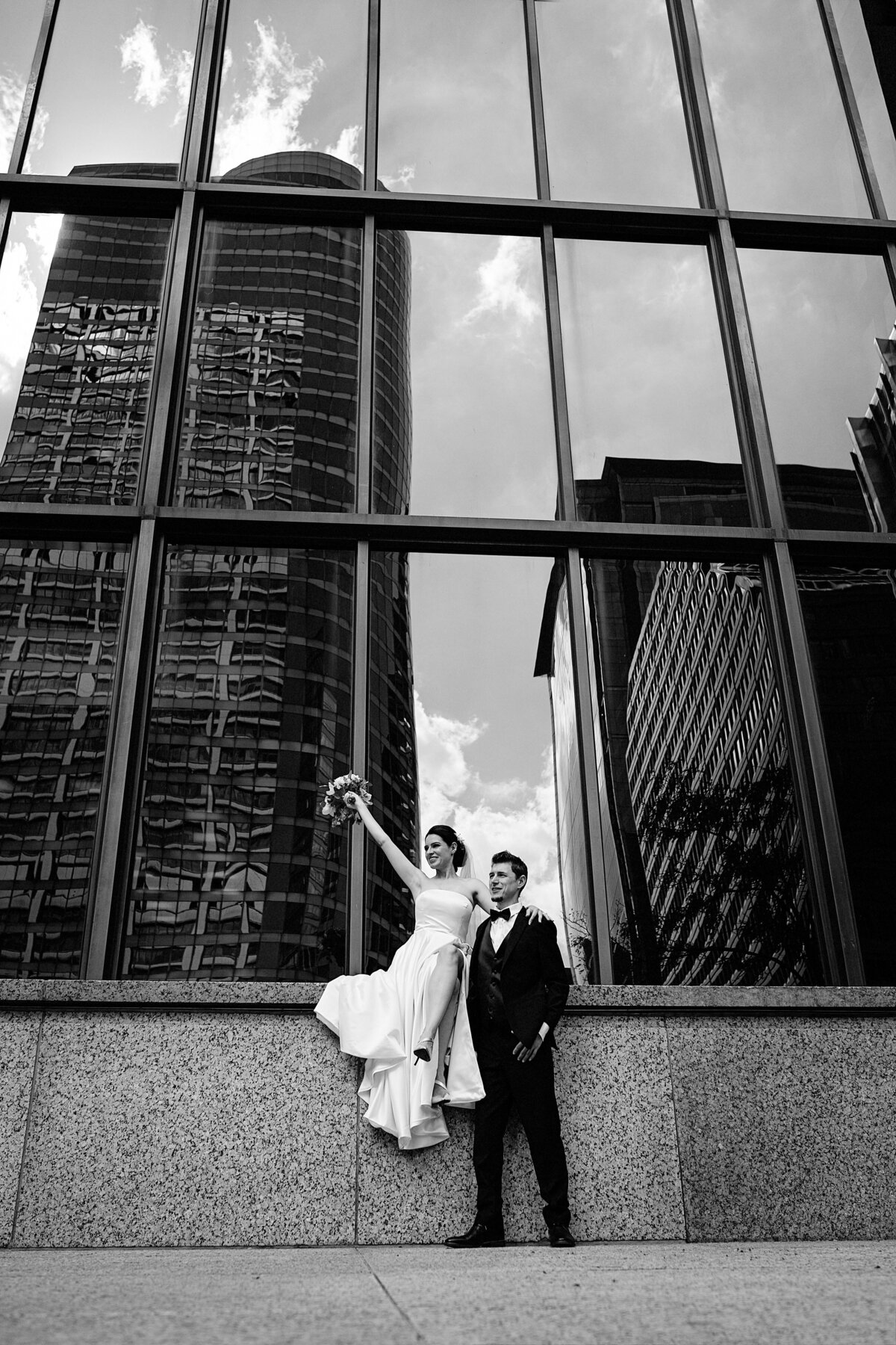 Newlyweds posing by tall Chicago building  with reflection of downtown on it