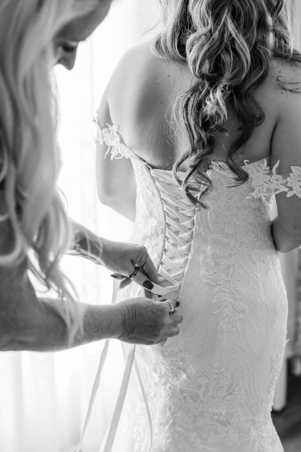 Black and white photo of mom tying daughter's wedding dress at Deep in the Heart Farms