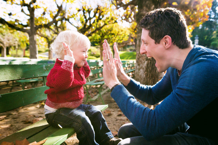 Candid shot of dad high fiving child sitting on a green bench