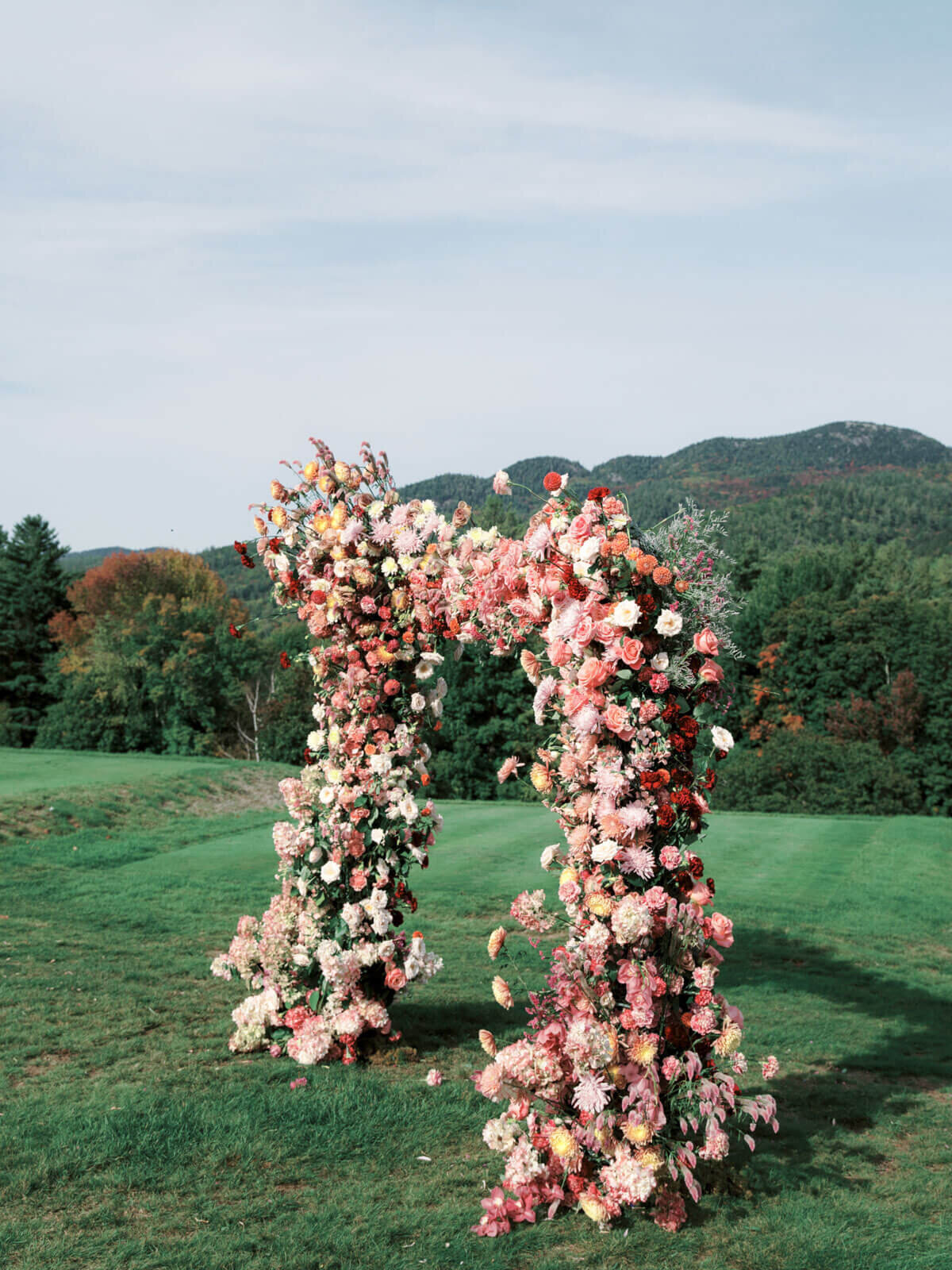 A beautiful wedding arch outdoors filled with flowers of peach, pink, red, and white hues. Image by Jenny Fu Studio.