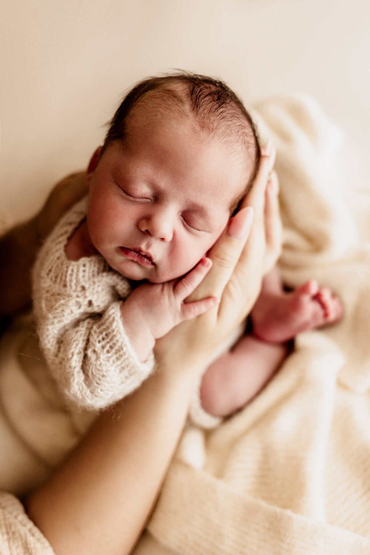 A mother holds her baby boy in her hands on a cream blanket.