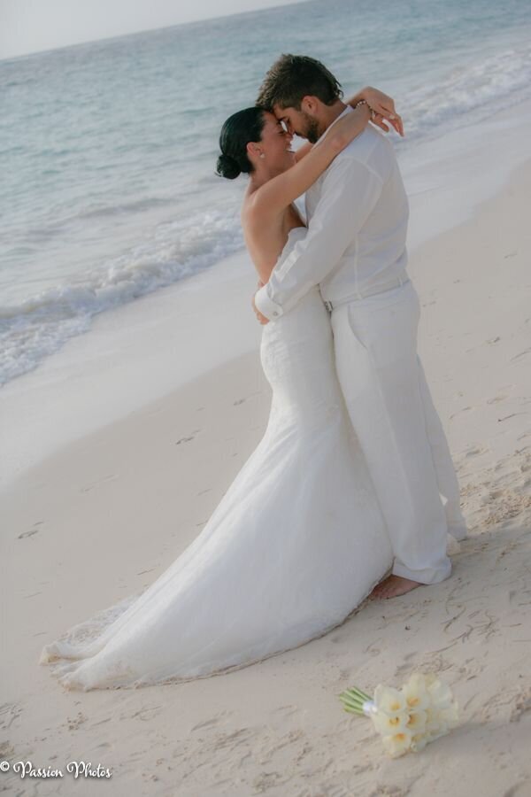 A couple embraces warmly on a sandy beach with the ocean in the background, capturing a tender and romantic moment. This image exemplifies the charm and intimacy of destination weddings, showcasing the stunning natural settings where love stories unfold.