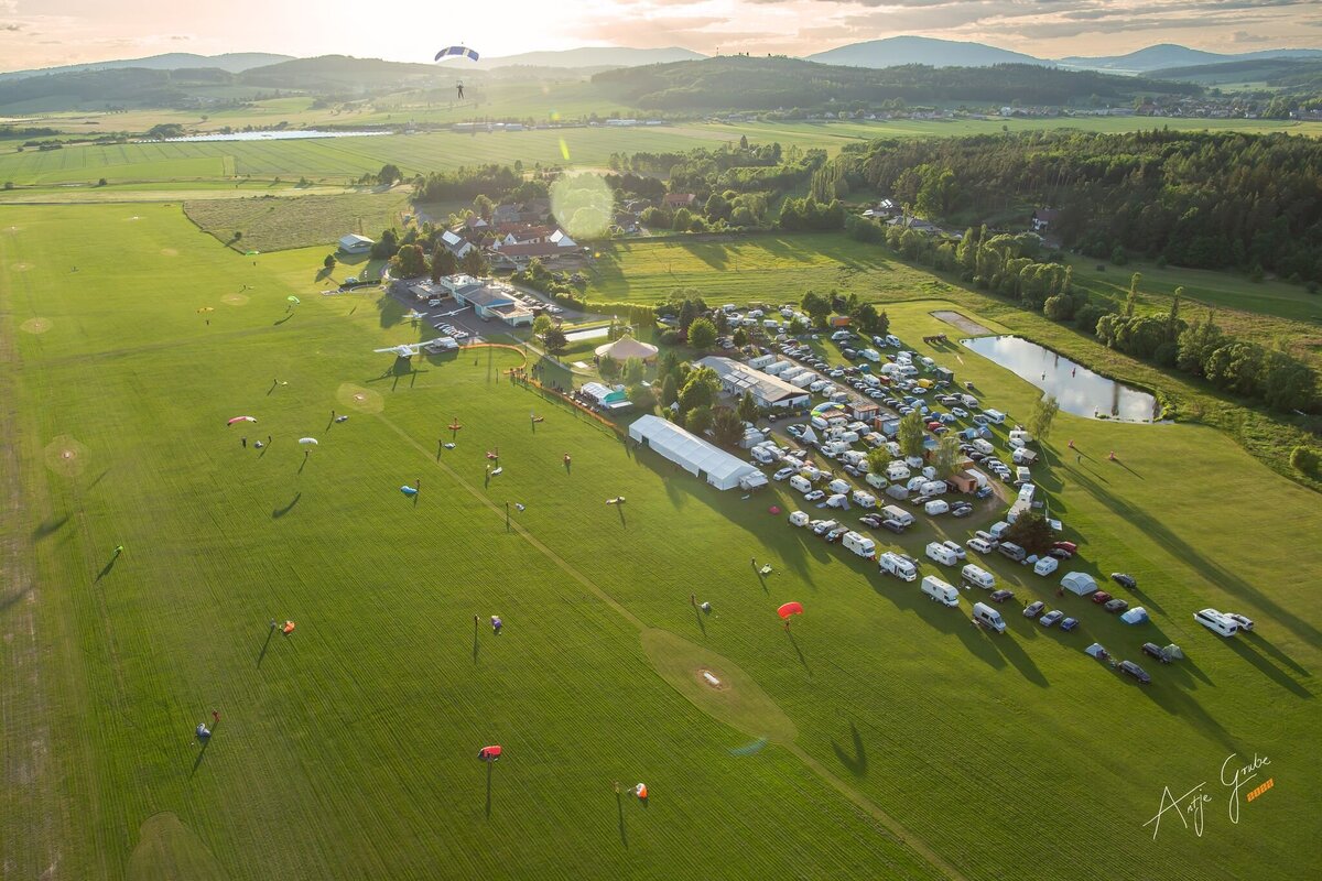 Das Bild zeigt den Sprungplatz in Klatovy von Oben. Es ist die grüne Wiese und der Camping Platz zu sehen während Fallschirmspringer landen