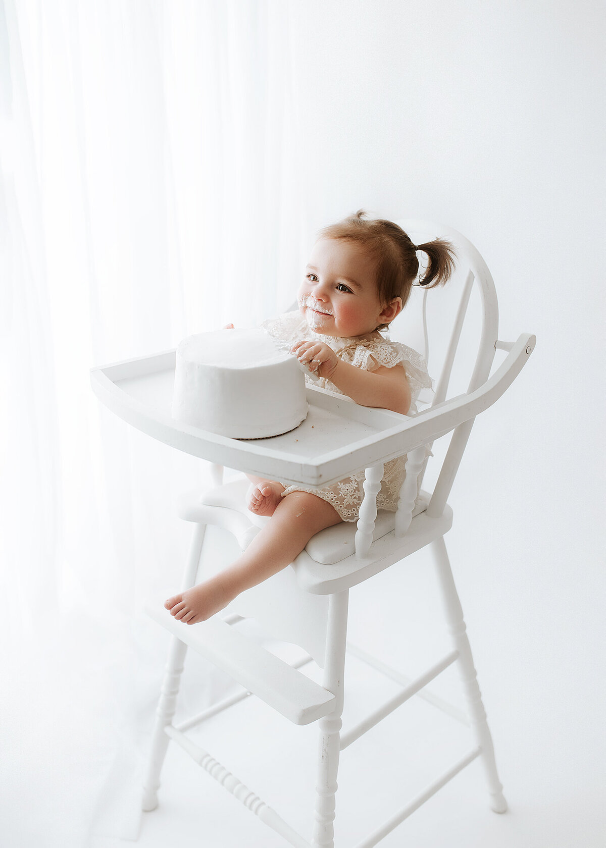 baby sitting in a white high chair, smiling at the camera for her first birthday photos near baldwinsville
