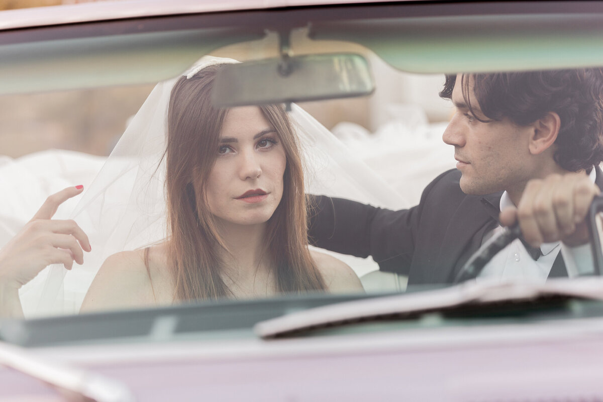 Close-up of couple seated in convertible, framed through the windshield.
