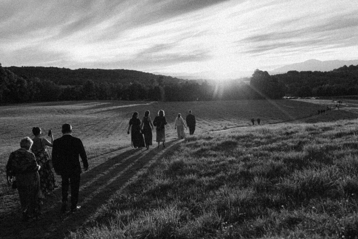 Des invités quittent vers la réception de mariage au coucher de soleil avec les montagnes comme décor, image en noir et blanc. 