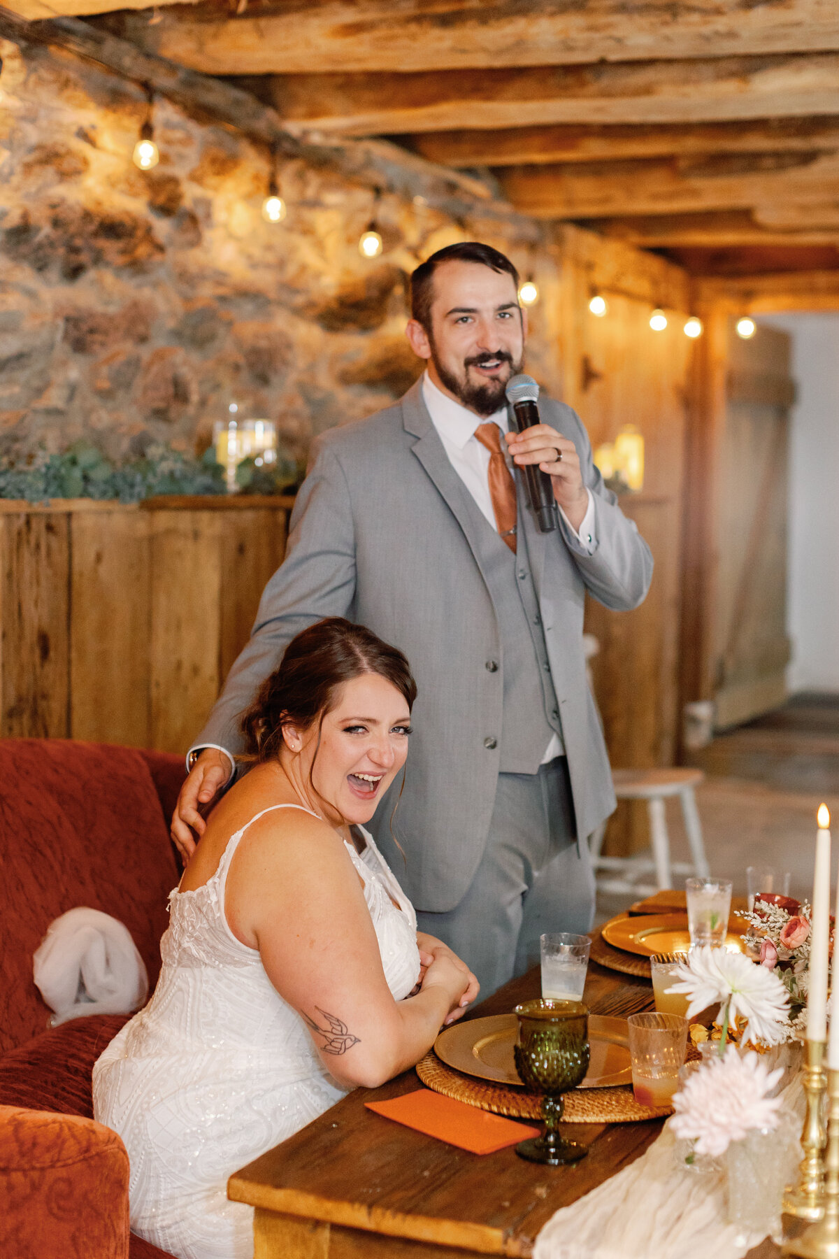 Groom giving toast at rustic barn reception surrounded by family and friends.