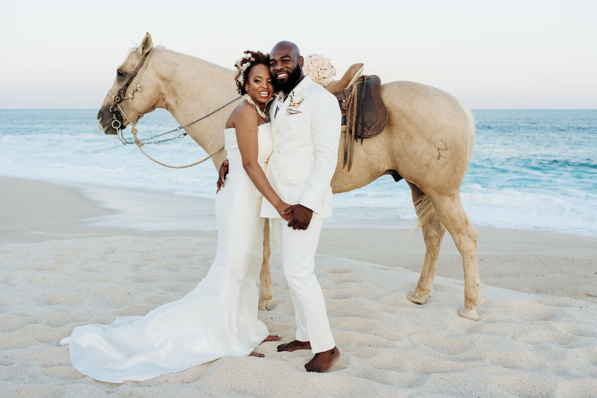 Bride and groom with a horse on the beach at sunset
