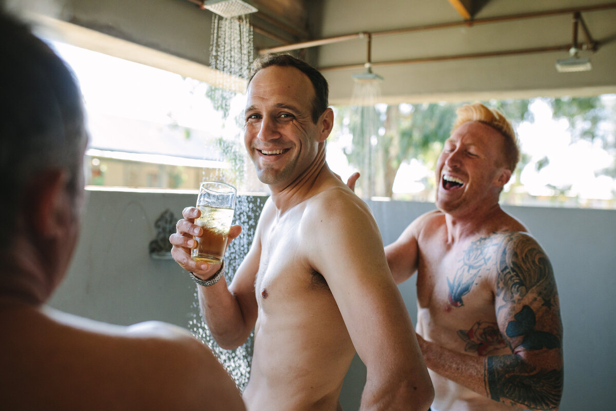 Candid moment of the groomsmen celebrating in the shower, one breaking into laughter while holding a drink.