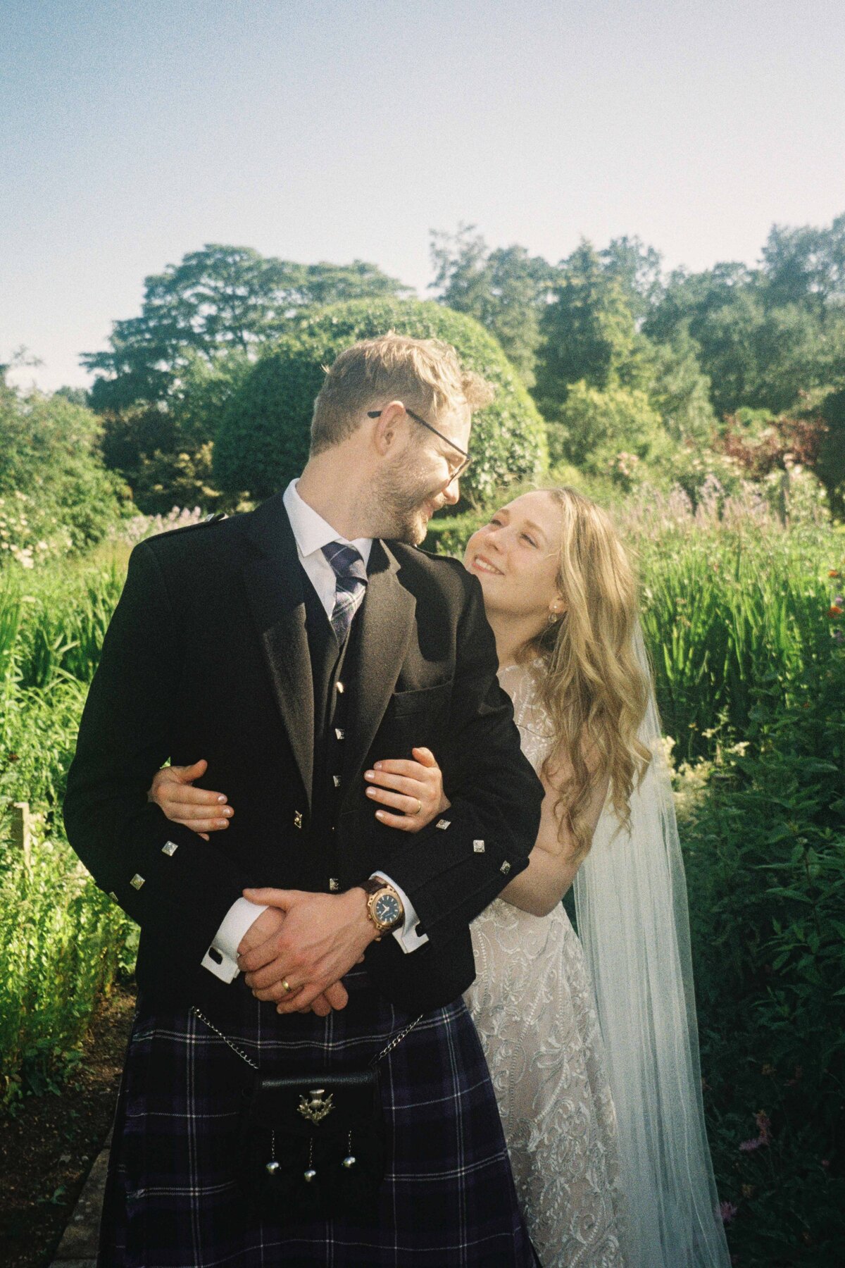 A bride wraps her arms around her groom from behind and they are photographed on 35mm film after their wedding.