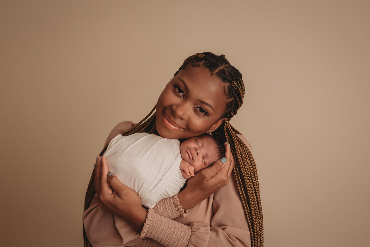 newborn pictures in Marietta Georgia at Maternity and Newborn Studio of Atlanta with  mom wearing a blush color dress and holding her newborn son snuggled close to her face swaddled in cream fabric