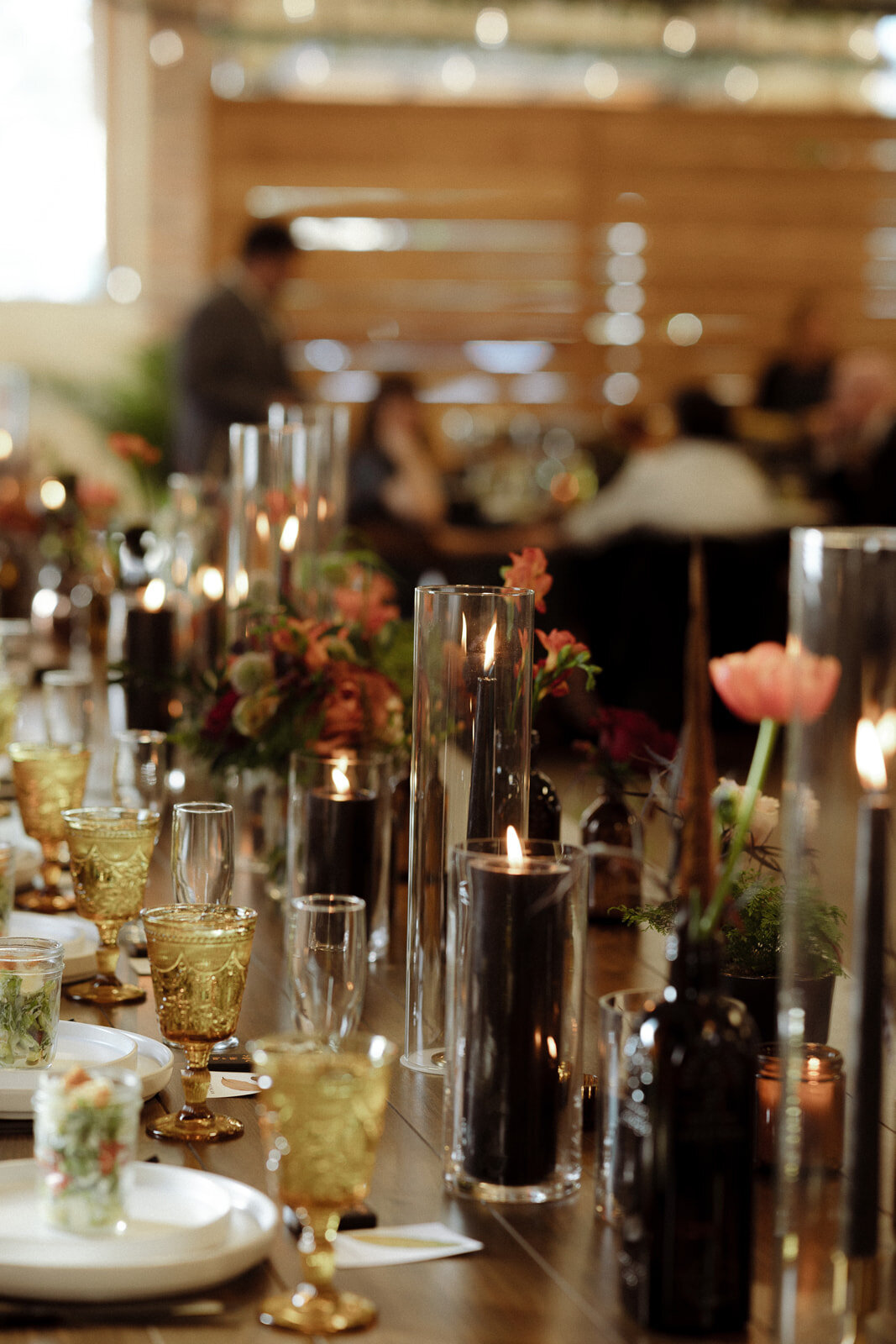 Amber glasses, black candles, and peach flowers on tables at a wedding reception in Colorado.