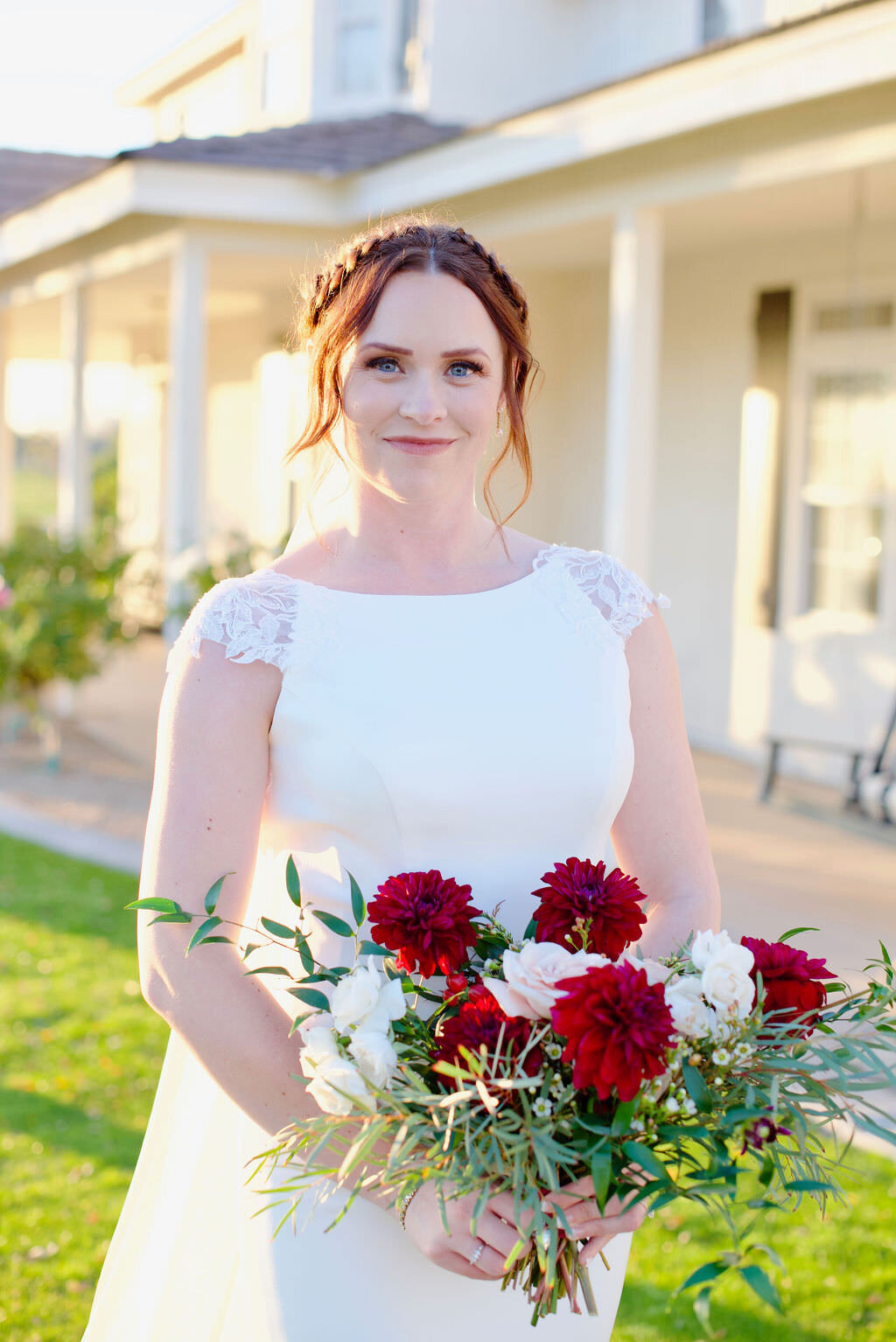 A bride smiling and holding a red and white bouquet of flowers.