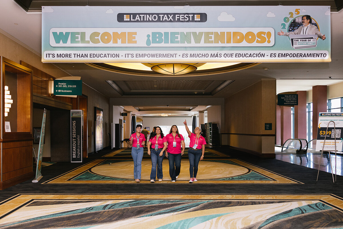 4 women walking under a welcom sign as one women points at it