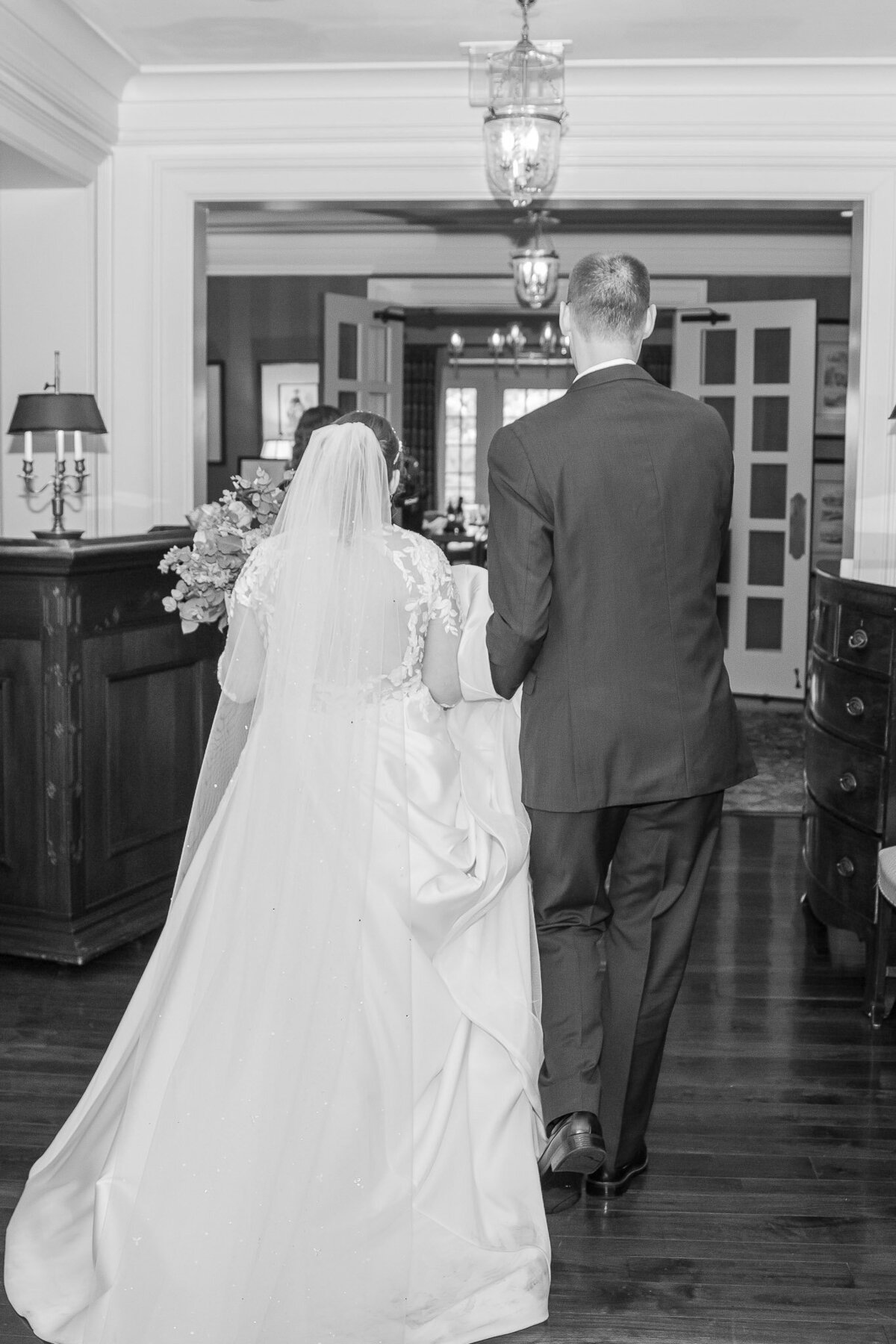 A photo of the bride and groom with their backs facing the camera. They are standing inside of a normal house on their wedding/elopement day.